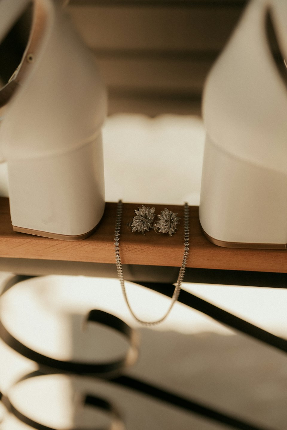 White high heels and diamond jewelry on a wooden shelf.