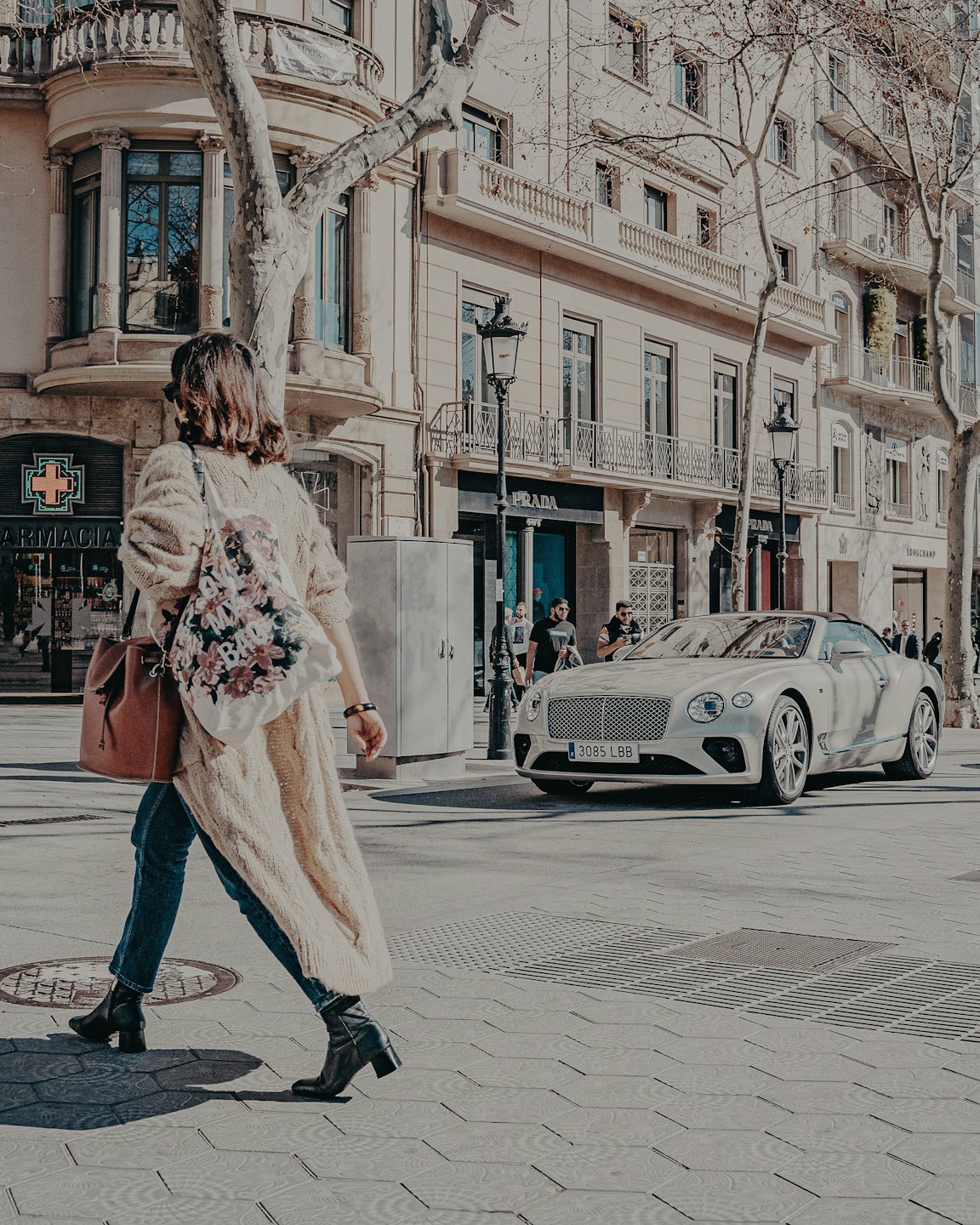 Woman walking past luxury storefronts carrying two handbags.